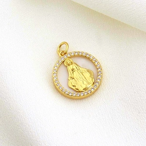 Detail of gold Virgin Mary pendant with clear zircon frame on white silk background
