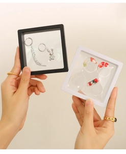 Hand holding square PE film jewelry frame showing a floating silver pendant inside