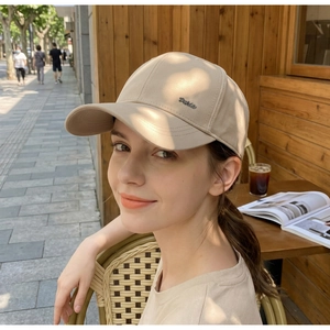 Detail of metal letter logo on beige cotton baseball cap worn in a cafe setting