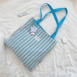 Dettaglio della borsa tote a righe blu con ciondolo a fiore di peluche e logo