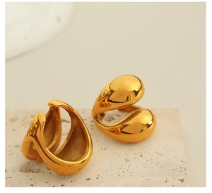 Close-up of chunky gold-plated teardrop earrings displayed on a textured stone pedestal