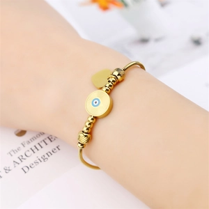 Close-up of gold snake chain bracelet with evil eye and heart charms on woman's wrist