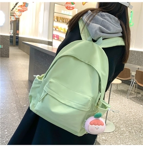 Rear view of a mint green minimalist backpack with a pink plush charm on a model
