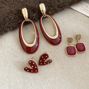 Detail of dark red heart and geometric enamel earrings on a beige textured surface