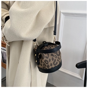 Detail of leopard print woven crossbody bucket bag with black leather trim on a model
