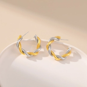 Two-tone twisted C-shape earrings in gold and silver plating on white ceramic plate