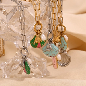 Close-up of enamel shell pendants with pearls on gold and silver chains over glass