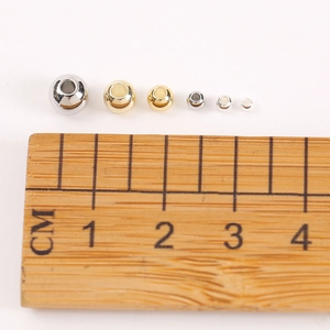 Polished 18K gold and silver plated copper beads in multiple sizes on a scale ruler