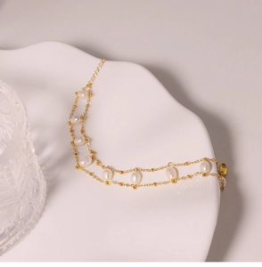 Detail of elegant double-layered golden chain bracelet featuring natural pearls on a white tray