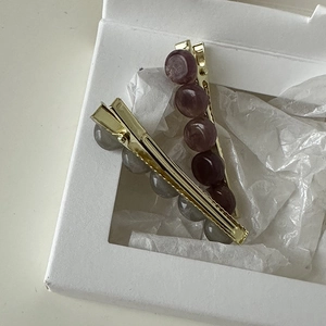 Detail of two beaded hair clips in deep purple and grey on gold metal ducksbill base