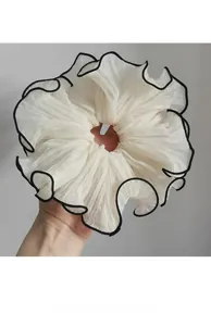 Detail of a large cream chiffon scrunchie with elegant black edge contrast and soft pleats
