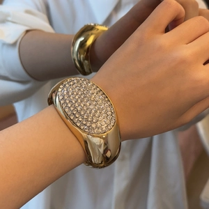 Luxuriöser breiter goldener Manschettenarmreif mit weißen Kristallen am Handgelenk eines Models