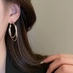 Detail of layered gold hoop earrings with textured facets on a model's ear