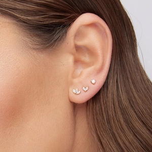 Detailed view of three gold 925 silver stud earrings with clear zircons on model's ear