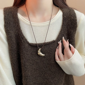 Detail of a golden croissant pendant on a leather cord over an autumn sweater