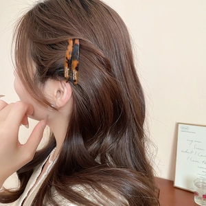 Dettaglio di due fermagli per capelli in acrilico tartarugato indossati lateralmente
