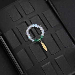 Detail of beaded ring with iridescent gems and a delicate gold feather charm pendant