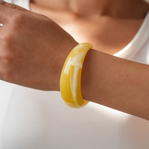 Close-up of a wide yellow marble acrylic cuff bracelet worn on the wrist with white outfit