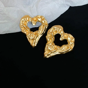 Detailed close-up of golden hollow heart earrings with lava texture on minimalist background