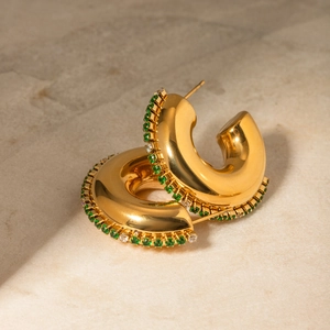 Macro detail of gold-plated thick hoop earrings with green and white cubic zirconia accents