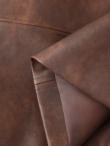 Détail de la texture en similicuir marron foncé et des coutures professionnelles sur la veste