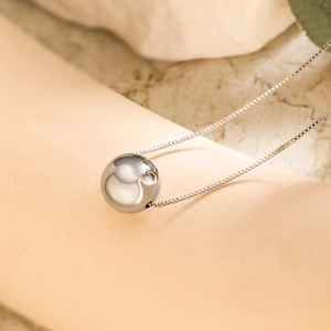 Close-up of a polished silver ball pendant on a fine metal chain with soft lighting
