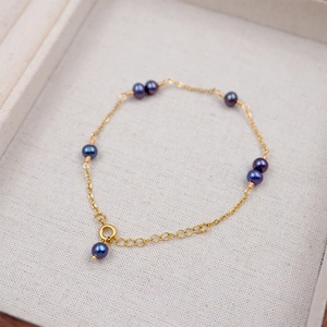 Elegant gold chain bracelet with deep purple pearls on a soft jewelry display tray