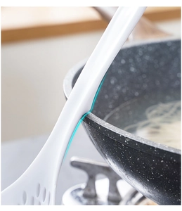 Detail of white kitchen skimmer with a non-slip hook resting on a cooking pot rim