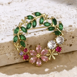 Close-up of golden wreath brooch with sparkling green and pink zircons on stone texture