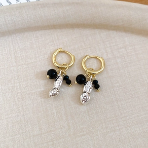 Close-up of golden hoop earrings with silver peanut charms and black beads on tray