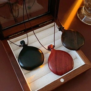 Three pear-shaped wooden pendants in black, red, and brown within a premium gift box