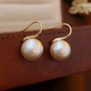 Gros plan de boucles d'oreilles dorées avec perles texturées sur cuir marron