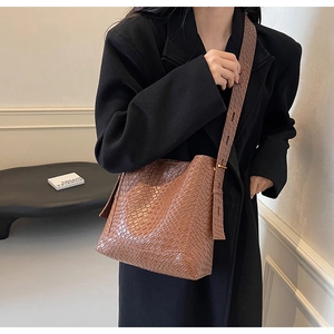 Close-up of brown woven bucket bag with wide adjustable shoulder strap on female model