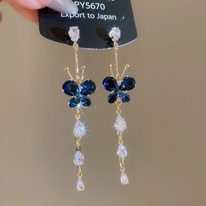 Detailed shot of gold earrings featuring blue butterfly gems and zircon drop tassels