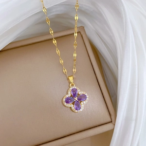 Macro shot of gold four-leaf flower pendant with purple stones on a beige jewelry box