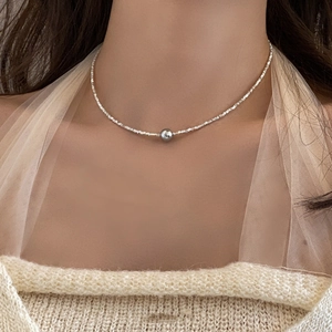 Close-up of minimalist silver necklace featuring a grey pearl on a woman's collarbone
