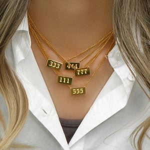 Vista detallada del collar superpuesto dorado con números de ángel y textura metálica.