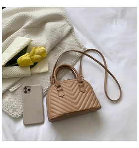Flat lay of brown shell handbag with V-quilted pattern next to yellow tulips