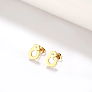 Detailed close-up of gold handcuff stud earrings with sparkling crystal inset on white surface