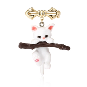 Detail view of a cute white cat on a brown branch brooch with golden bow accent