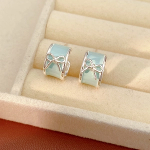 Detail of light blue bow hoop earrings with silver trim in a beige jewelry display tray