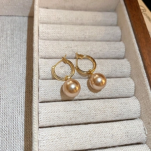 Gros plan de créoles dorées avec perles champagne dans un coffret à bijoux chic