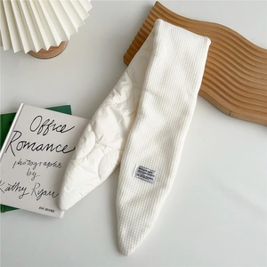 Close-up of a white quilted neck warmer with a creative label on a wooden tray