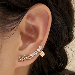 Close-up of golden Love cursive ear cuff with sparkling diamonds and pearl on ear