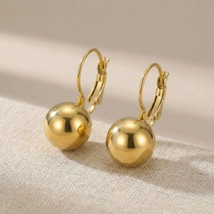 Detailed view of polished golden ball lever-back earrings on a textured background