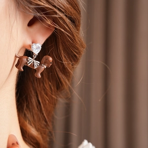 Close-up of a silver heart stud earring with a bow and brown dachshund puppy charm