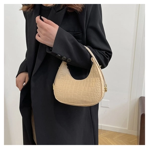Detail of a beige crocodile pattern crescent bag held by a model in a black blazer