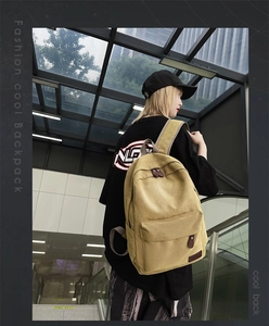 Model wearing a large khaki canvas backpack with front zipper pocket in street setting