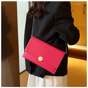 Dettaglio di una borsa a busta fucsia con fibbia dorata indossata su un blazer nero
