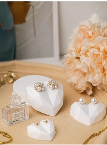 Detail view of pearl and heart earrings on a white heart-shaped jewelry display stand